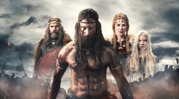 A viking with brown hair shirtless and with tattoos stood in front of the image with two female vikings and a male stood behind him against a stormy background in the movie The Northman