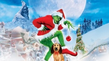 Green character dressed as Santa holding a red ornament in a snowy Whoville setting with a decorated Christmas tree and full moon.