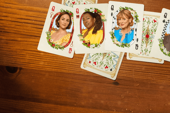 A spread of decorative playing cards featuring illustrated portraits on a wooden tabletop.