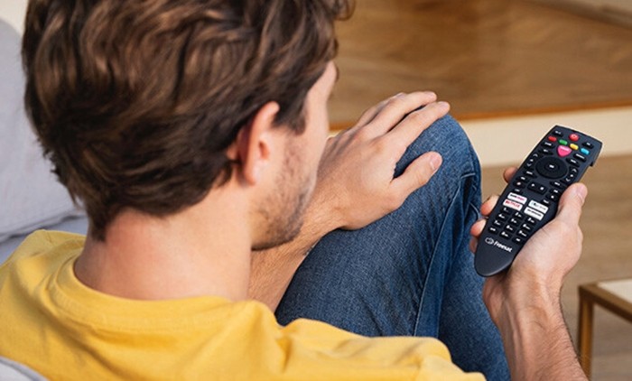 A photograph of a person holding a Freesat remote control