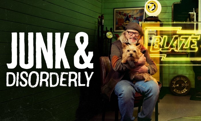 Person sitting in a vintage workshop holding a small dog beside a neon Blaze sign, surrounded by retro collectibles.