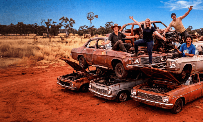 Four people stood on a pile of old rusty cars in the Australian Outback for the show Outback Wreckers