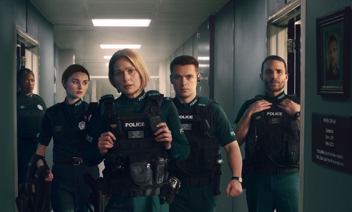 Blue Lights TV drama cast members in police uniforms inside a station corridor during a tense scene.
