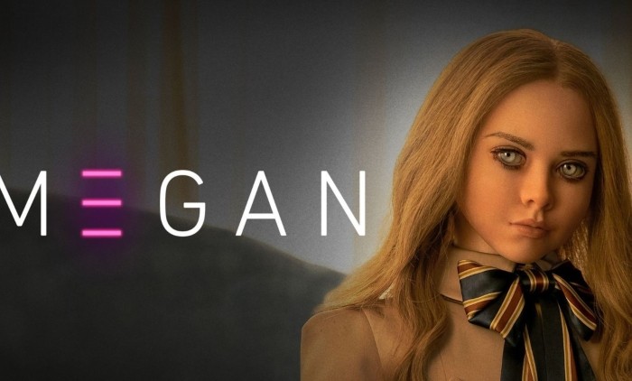 Promotional image for M3GAN featuring the lifelike AI doll M3GAN with long blonde hair, a beige outfit and striped bow tie, set against a dark background. The sci-fi horror film explores artificial intelligence, robotics and the dangers of advanced companion technology.