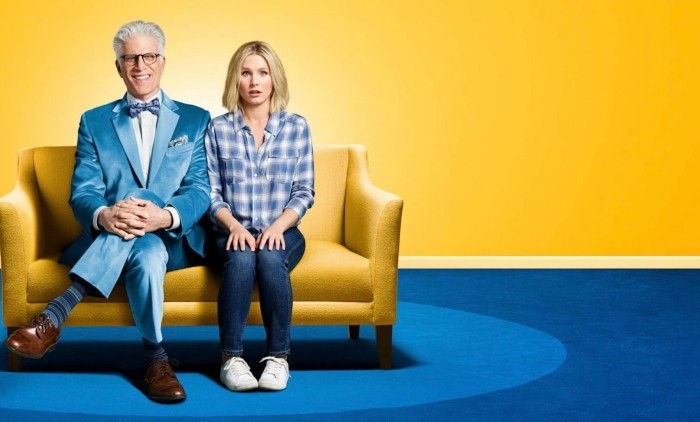 A man and a women wearing blue sat on a yellow sofa on blue carpet against a yellow background. Key art image for The Good Place.