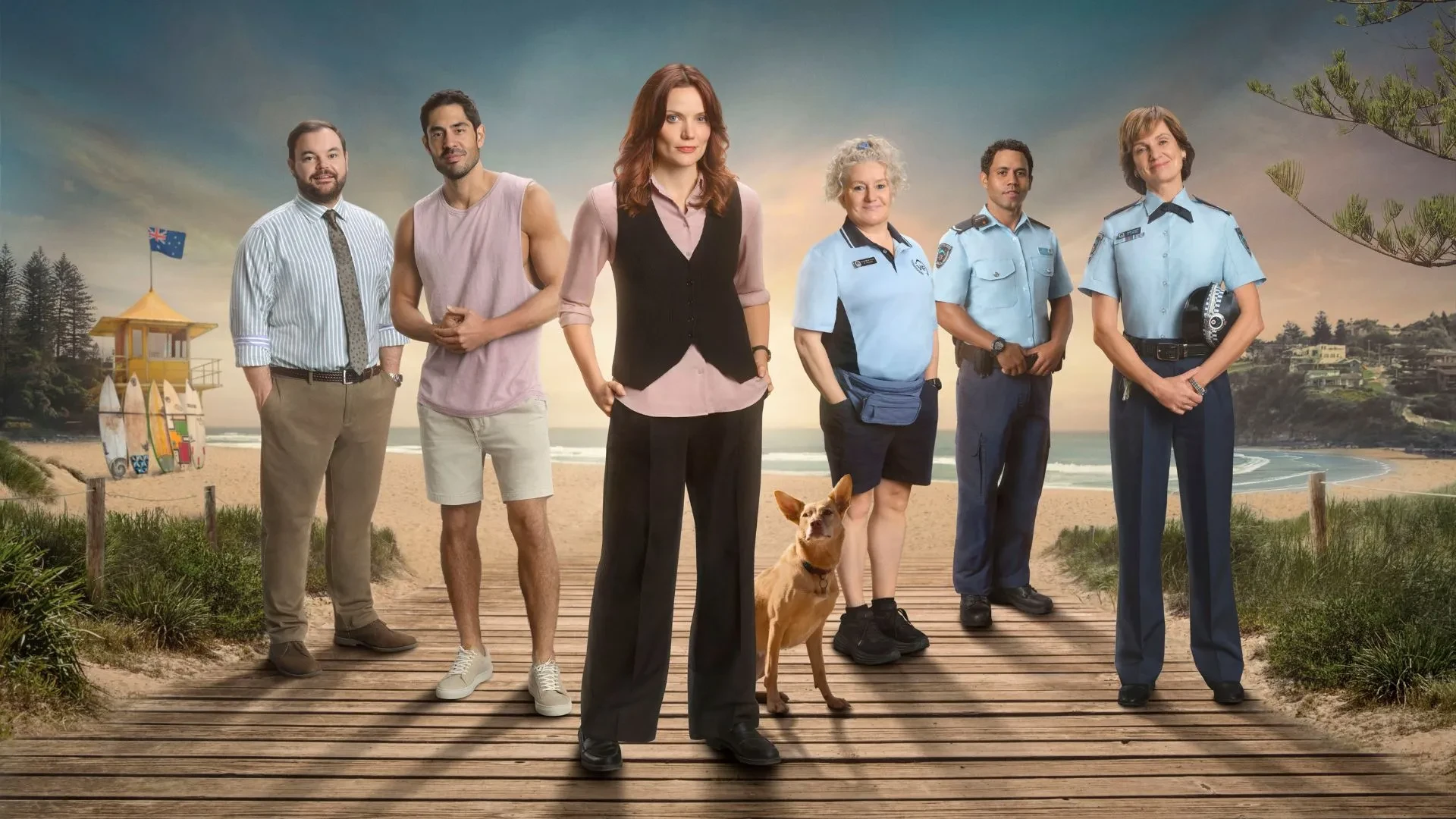 Catherine McClements and other cast members stood on a beach in uniform with a dog stood behind her in the drama Return to Paradise