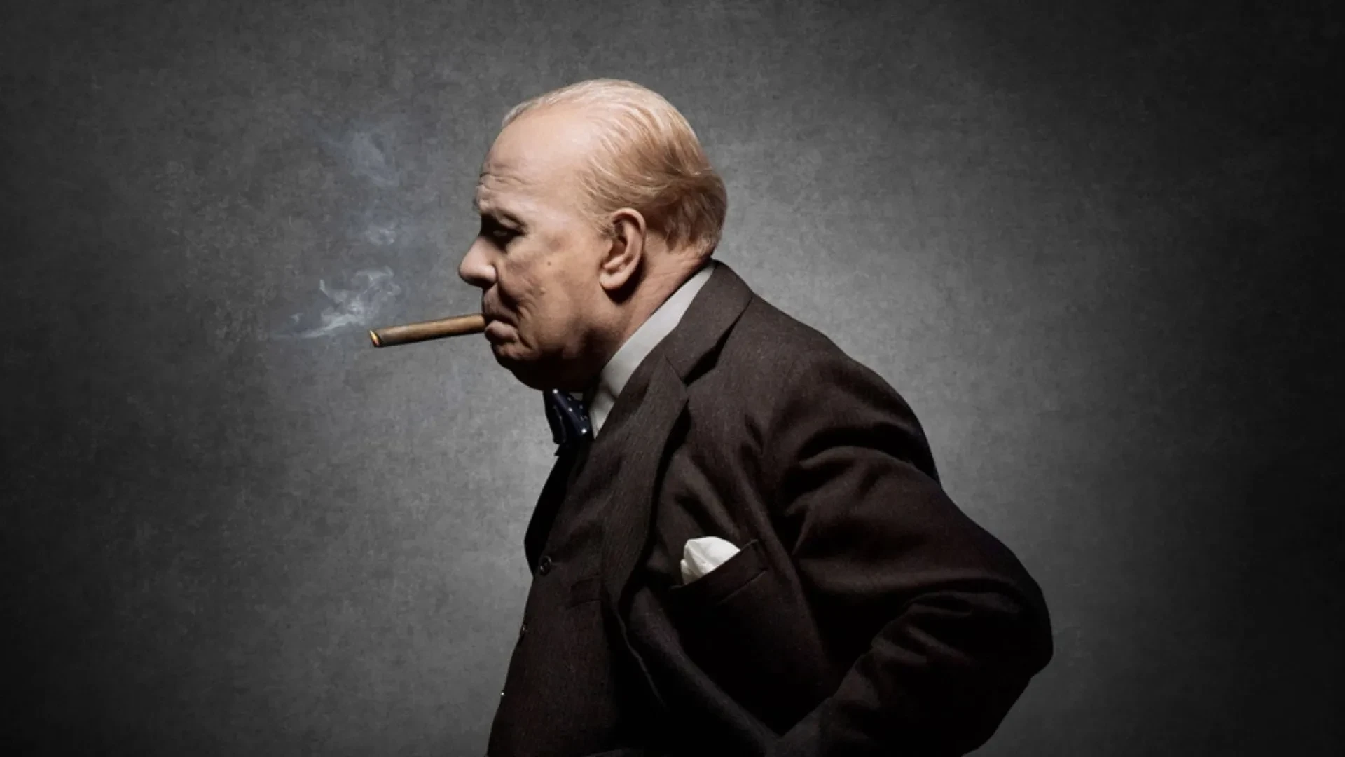 Gary Oldman as Winston Churchill smoking a cigar in a black suit in the movie The Darkest Hour
