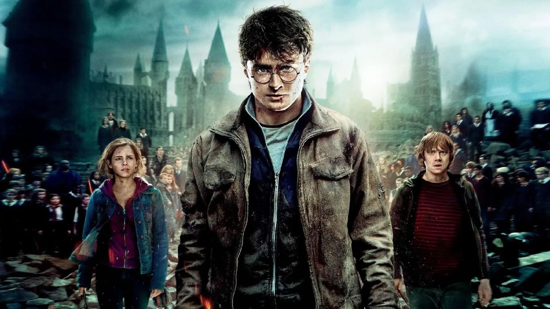 Daniel Radcliffe stood in an a shabby jacket in front of the backdrop of Hogwarts castle with Rupert Grint and Emma Watson stood behind him