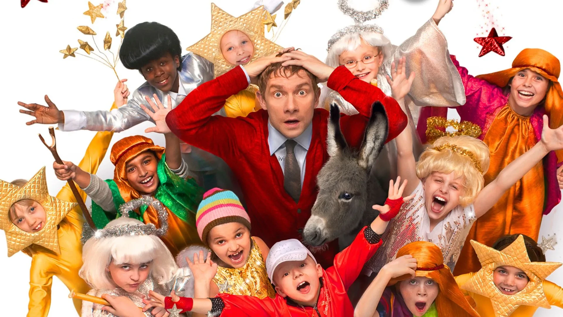 Colourful group of children in bright costumes with stars and festive props surrounding a donkey, representing a lively nativity play.