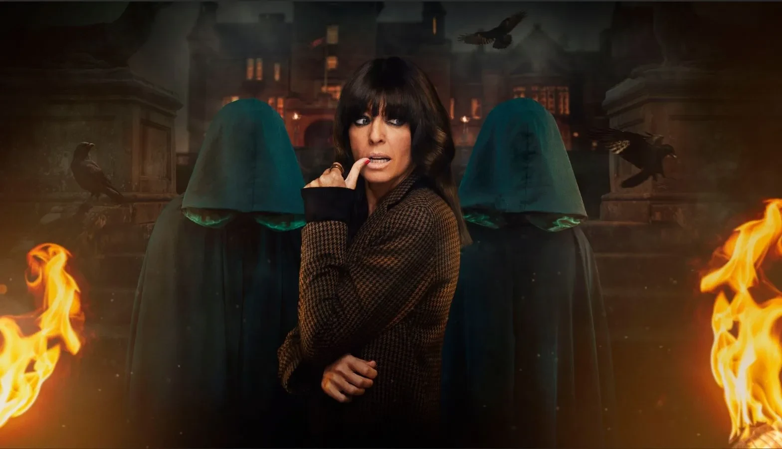 Promotional artwork for the TV series “The Traitors”, featuring Claudia Winkleman in the foreground wearing a dark checked coat, with two hooded figures standing behind her against a moody backdrop of a grand building, flames on either side, and crows flying overhead.