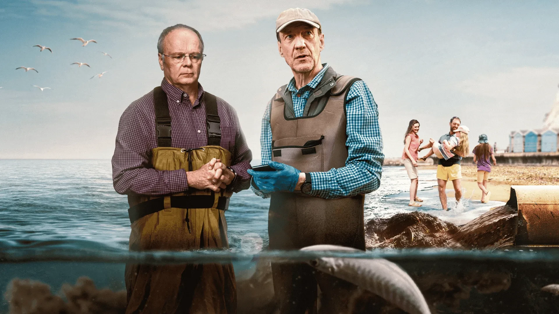 Two people wearing waders standing by the shoreline with fish visible underwater and families walking along the beach.