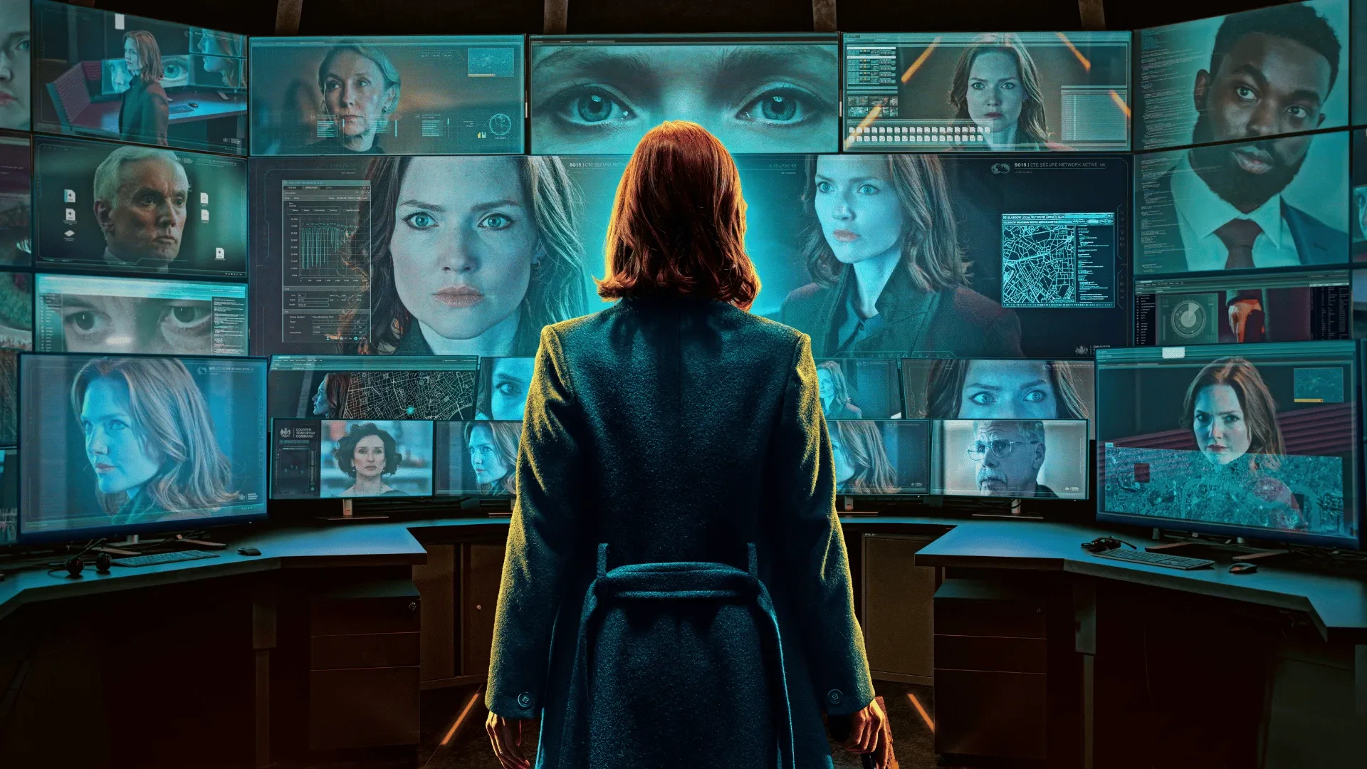 Person in a dark coat standing in front of multiple surveillance screens displaying security footage and digital data.