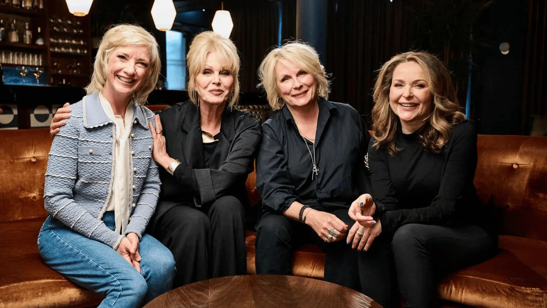 Four cast members seated together in a stylish bar setting, smiling on sofa, Absolutely Fabulous: Inside Out