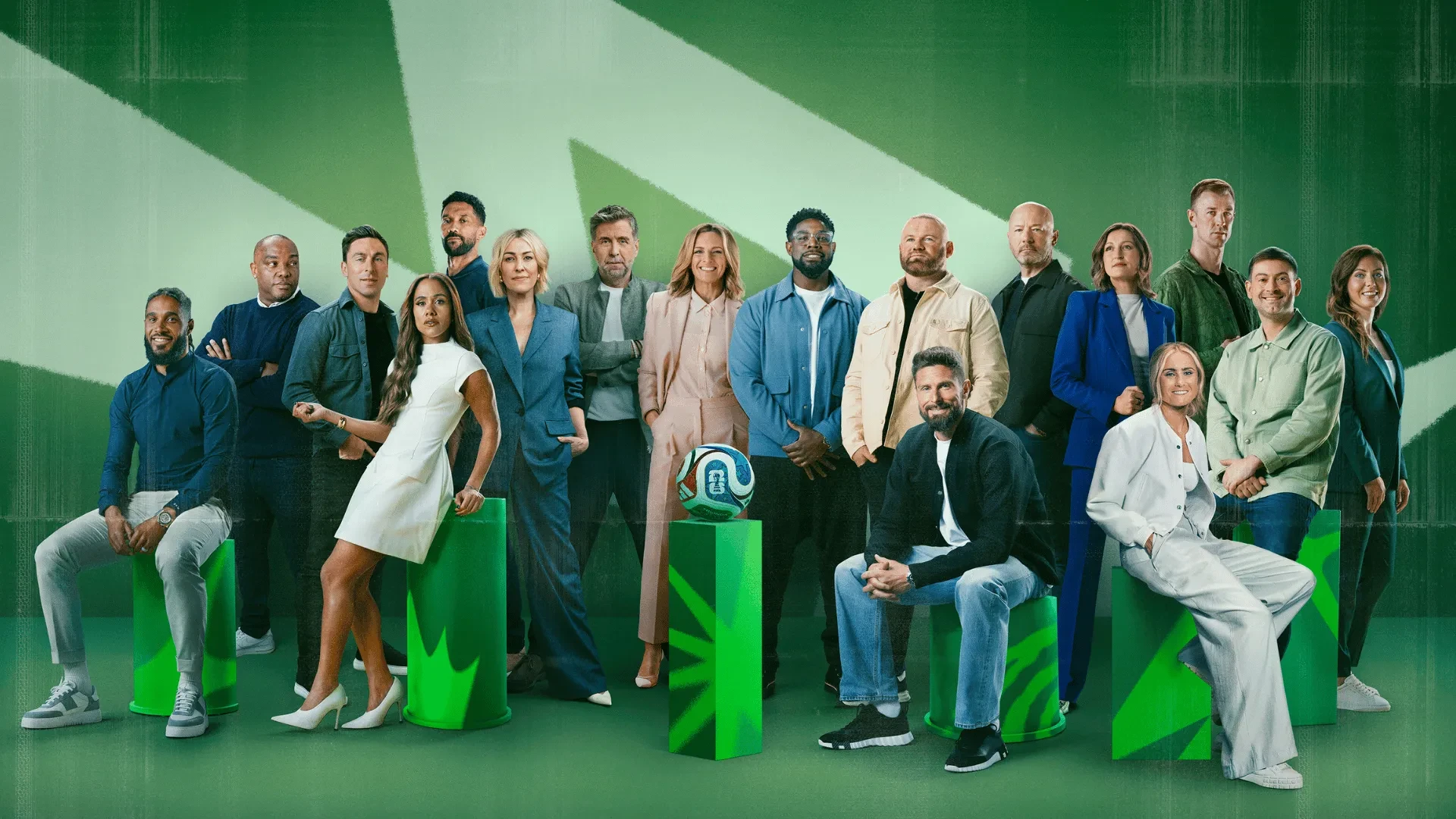 Large group of football personalities and presenters posed with a ball against a green graphic background, promotional image for FIFA World Cup coverage