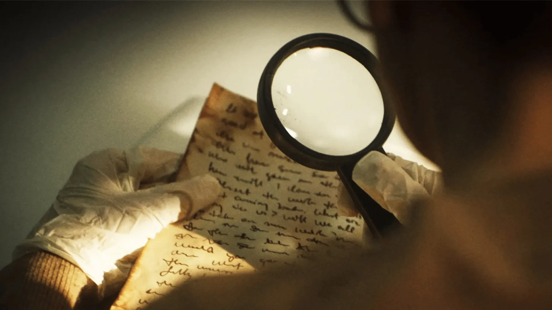 Gloved hands examining an old handwritten letter with a magnifying glass, mystery investigation close-up