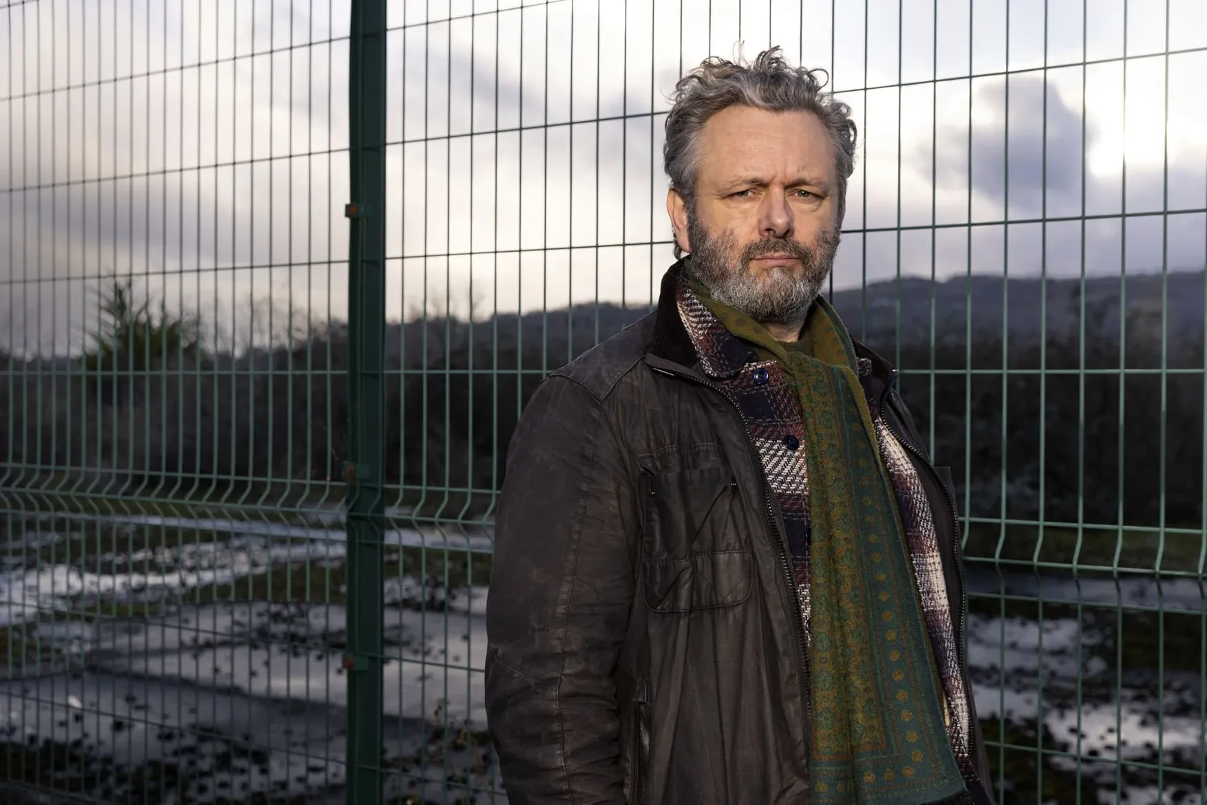 Promotional image for Buried: A Toxic Secret with Michael Sheen shows the actor standing by a fence