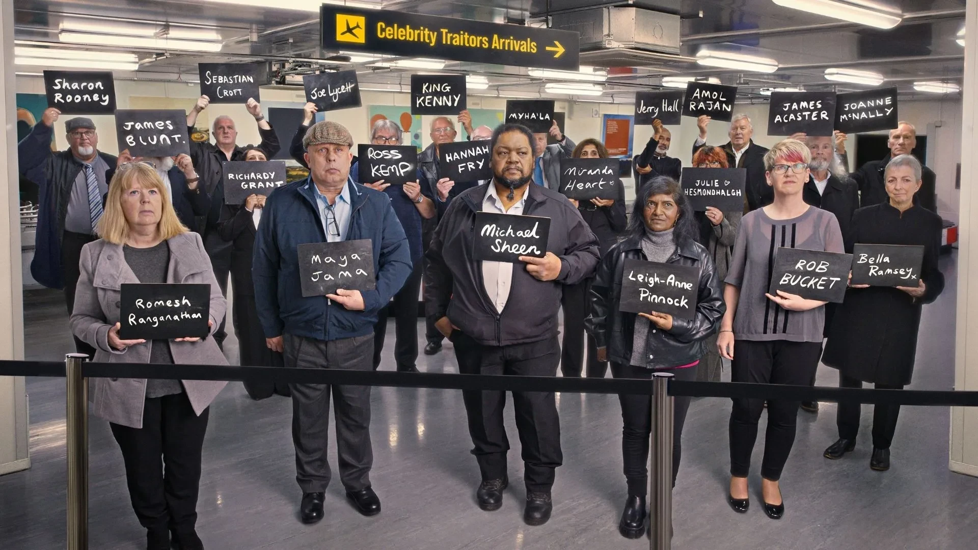 Promotional image for Celebrity Traitors showing contestants holding name boards in an airport arrivals area beneath a Celebrity Traitors Arrivals sign