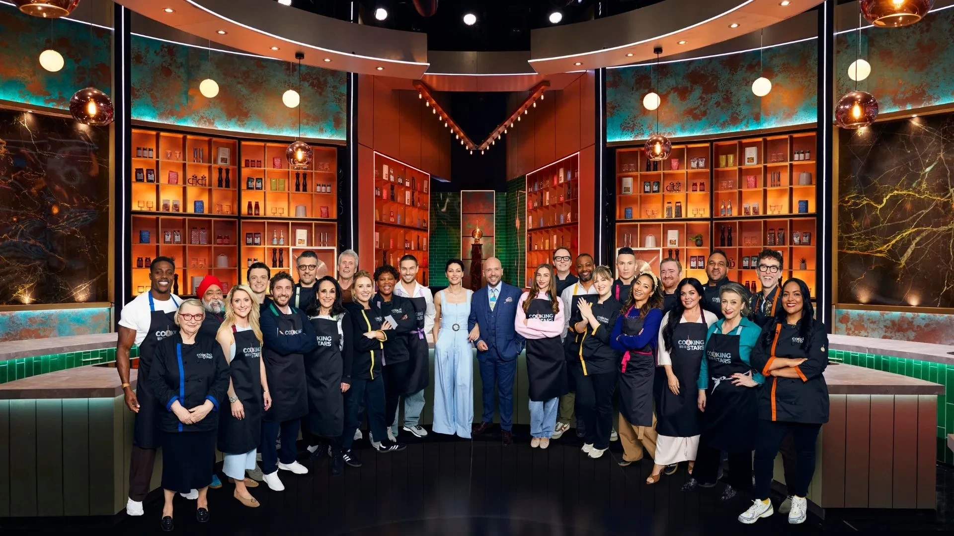 Posh kitchen style background with the competitors and judges of Cooking with the Stars stood in front of it.