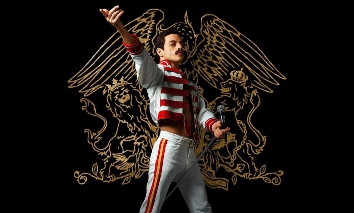 Rami Malek as Freddie Mercury wearing a stylish outfit against a black background with the Queen logo in gold
